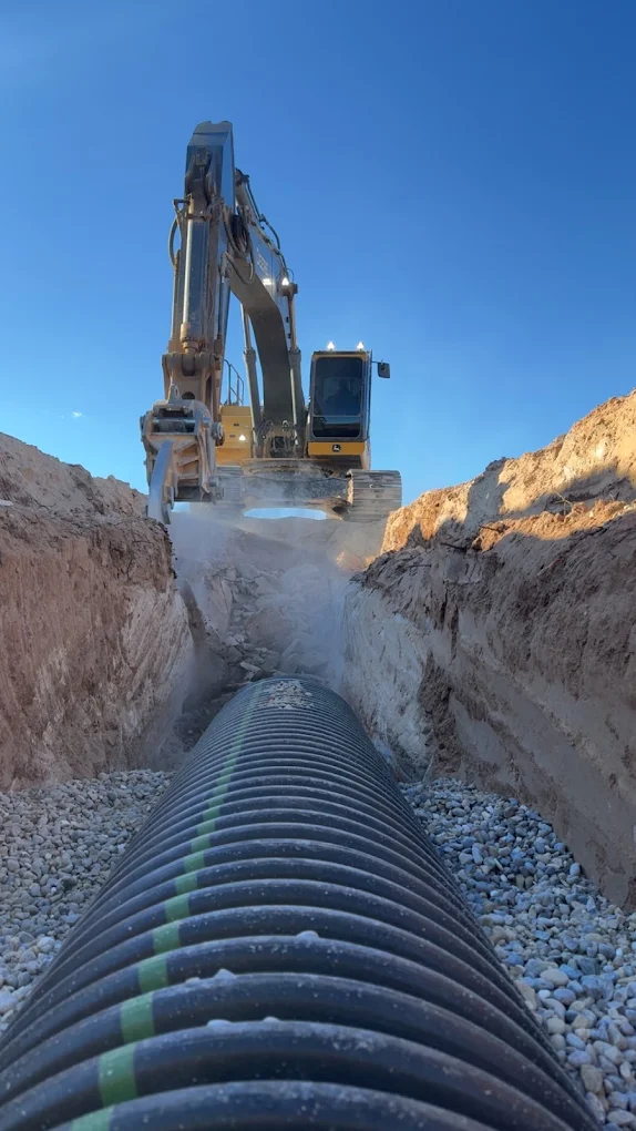 Excavator over trench with corrugated pipe